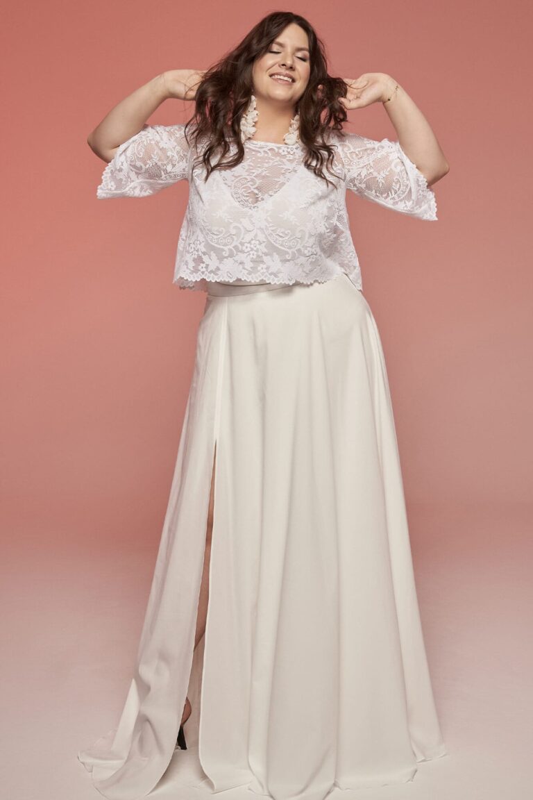 Suknia ślubna z długim rozcięciem i koronkową bluzką z rękawami.