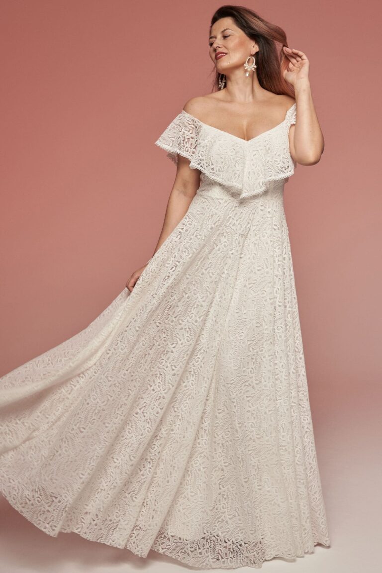Suknia ślubna z odkrytymi ramionami, długim dołem i koronkowymi detalami.