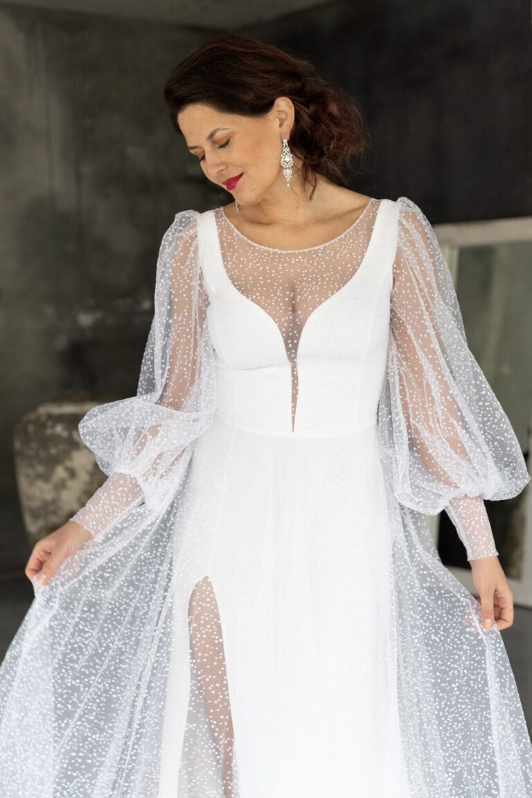 Suknia ślubna z długimi przezroczystymi rękawami i głębokim dekoltem.