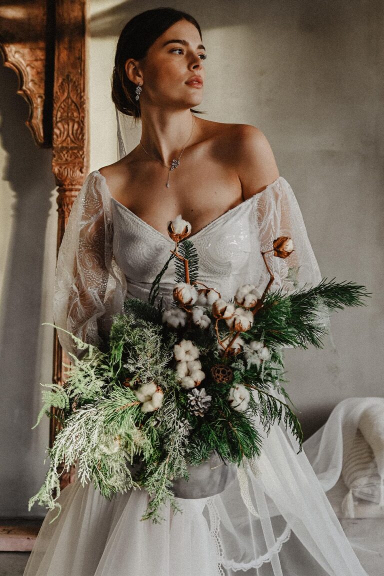 Suknia ślubna z dekoltem w serce, długimi koronkowymi rękawami i bukietem z bawełny oraz zieleni.