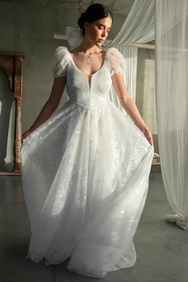 Suknia ślubna z dekoltem w serek, krótkimi rękawami i rozkloszowanym dołem.