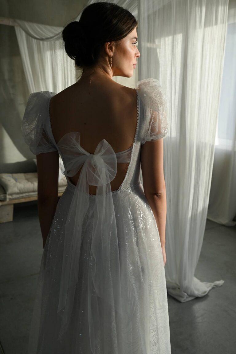 Suknia z odkrytymi plecami, tiulowymi rękawami i kokardą z tyłu.