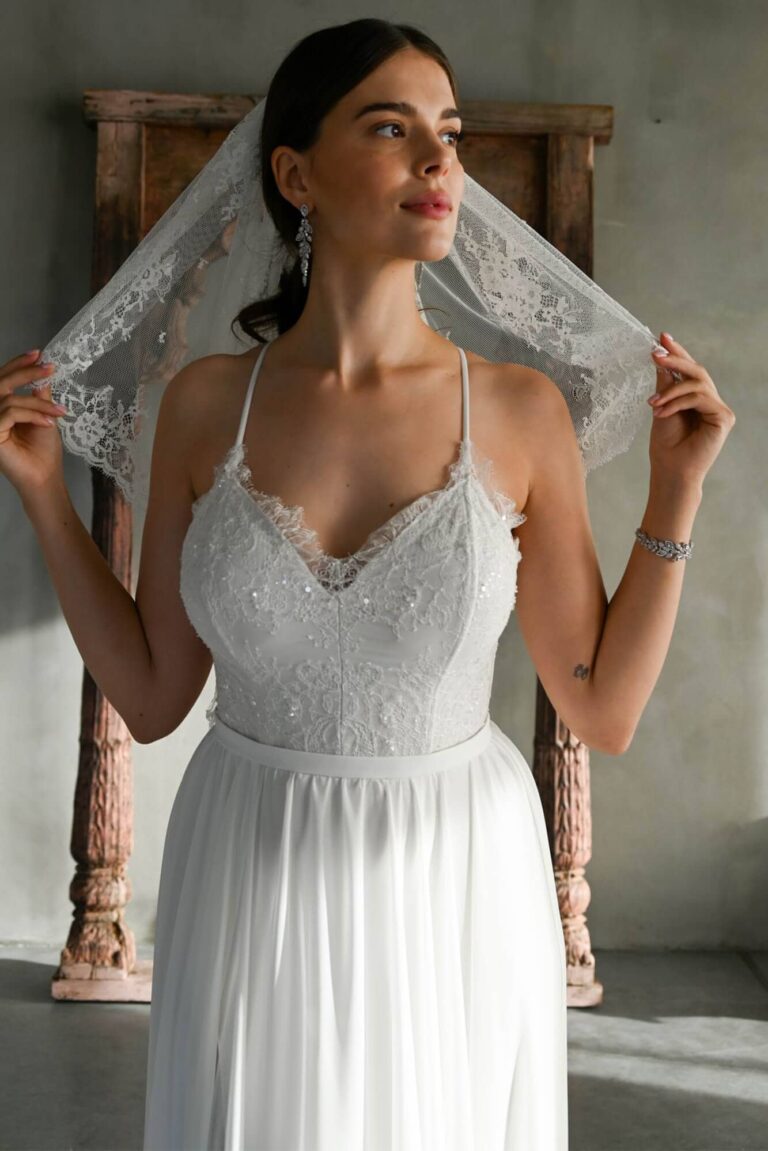 Suknia ślubna z koronkowym dekoltem i cienkimi ramiączkami, z długim welonem.