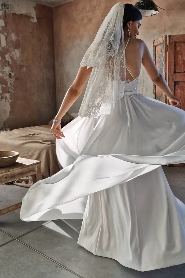 Suknia ślubna z odkrytymi plecami i długim trenem, z woalką na głowie.