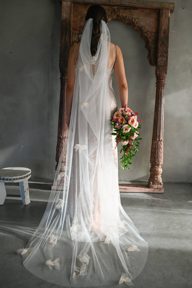 Suknia ślubna z długim trenem, odkrytymi plecami i tiulowym welonem.