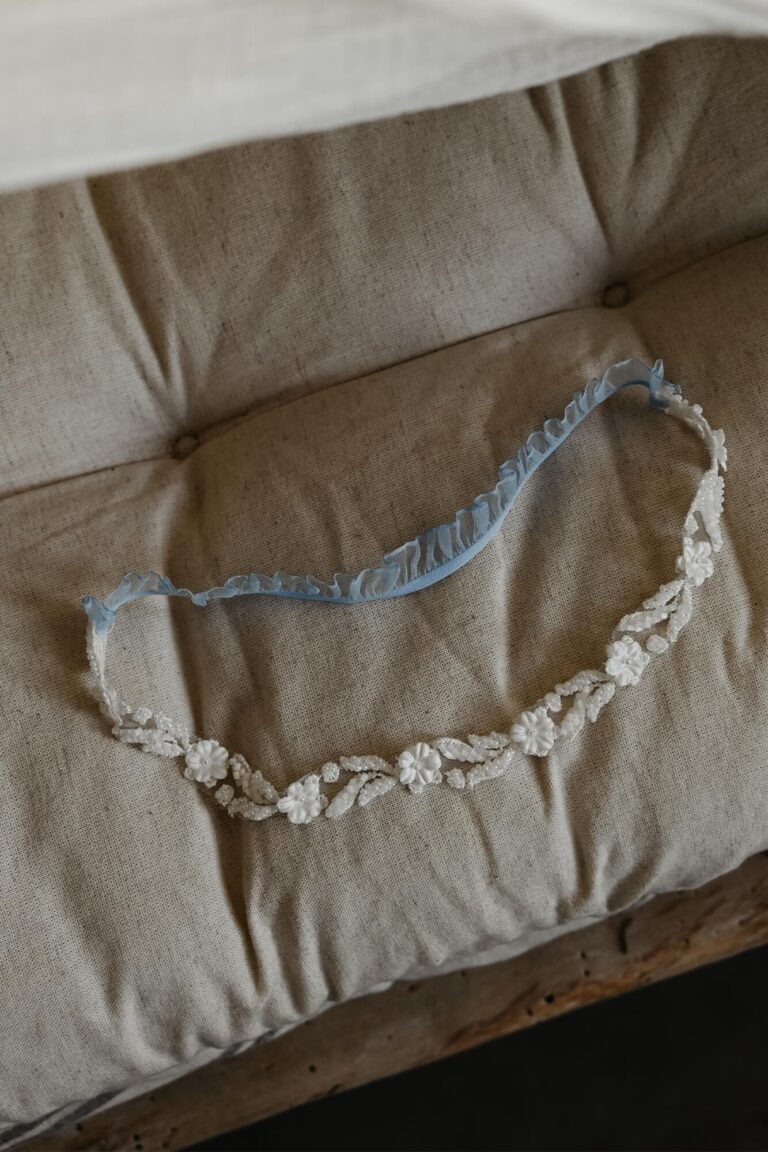 Podwiązka z białymi kwiatami i niebieską koronką na beżowym tle.