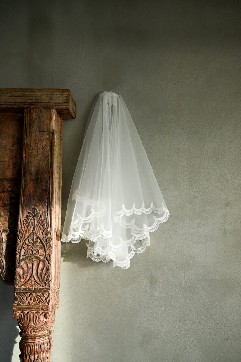 Zasłona w kolorze białym z koronkowym wykończeniem zawieszona na ścianie.