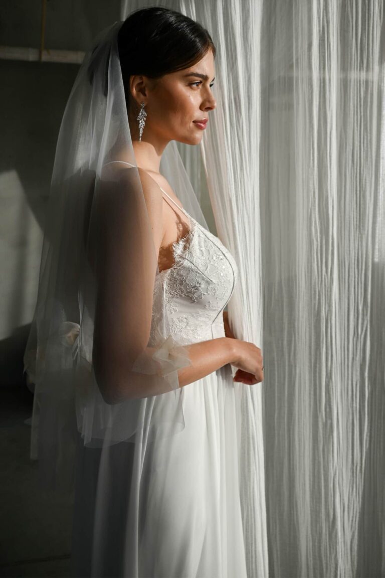 Suknia ślubna z koronkowym dekoltem i długim welonem, widziana z boku.