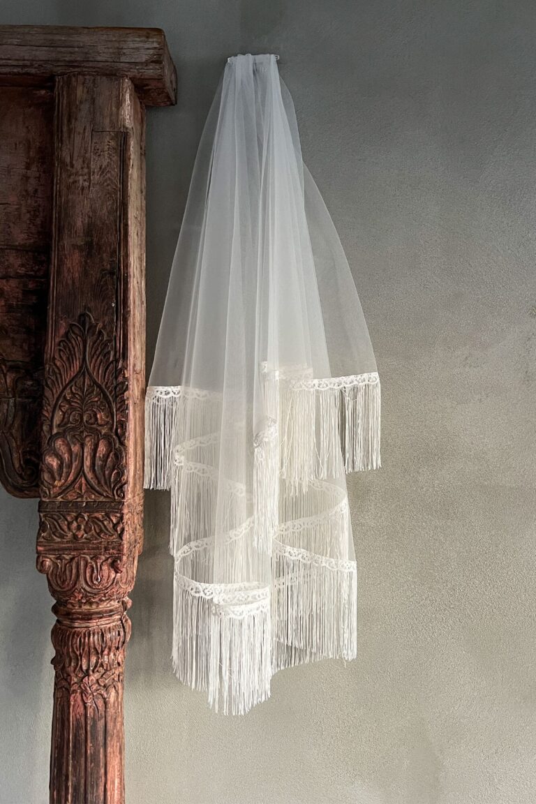 Suknia ślubna z długim welonem, wiszącym w pionie, z przezroczystego materiału.