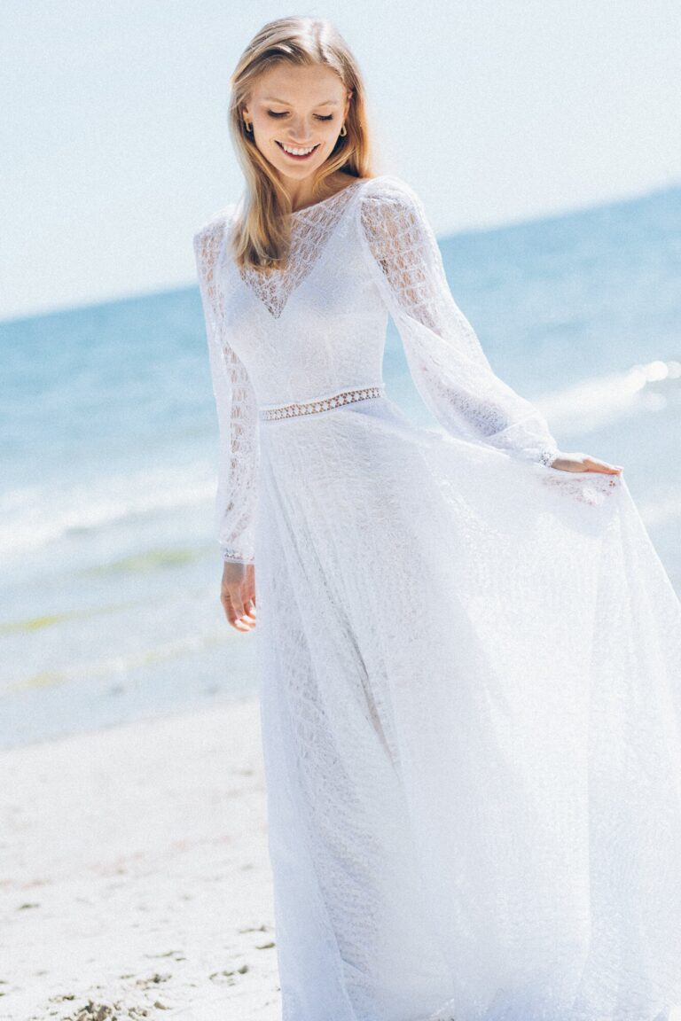 Suknia z długimi rękawami i zwiewnym materiałem widoczna na plaży.