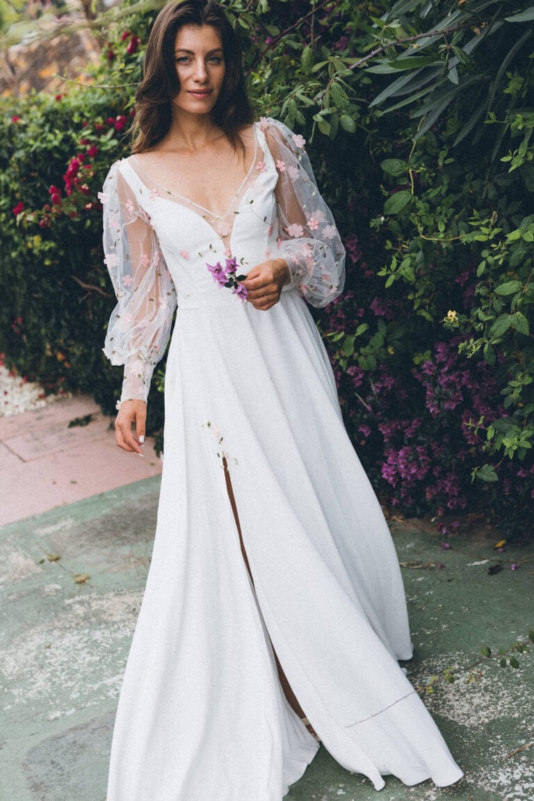 Suknia ślubna z długimi rękawami i głębokim dekoltem, z rozcięciem z przodu.