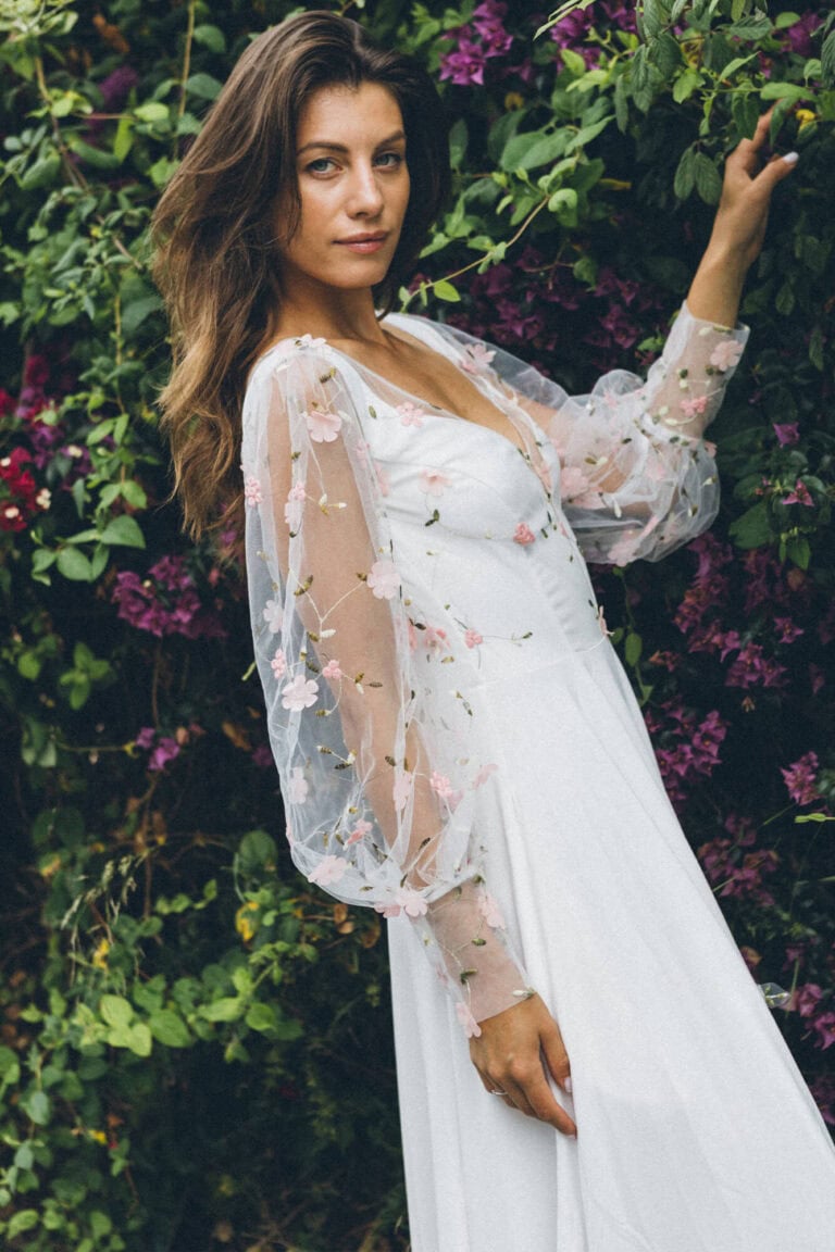 Suknia ślubna z długimi koronkowymi rękawami i głębokim dekoltem.