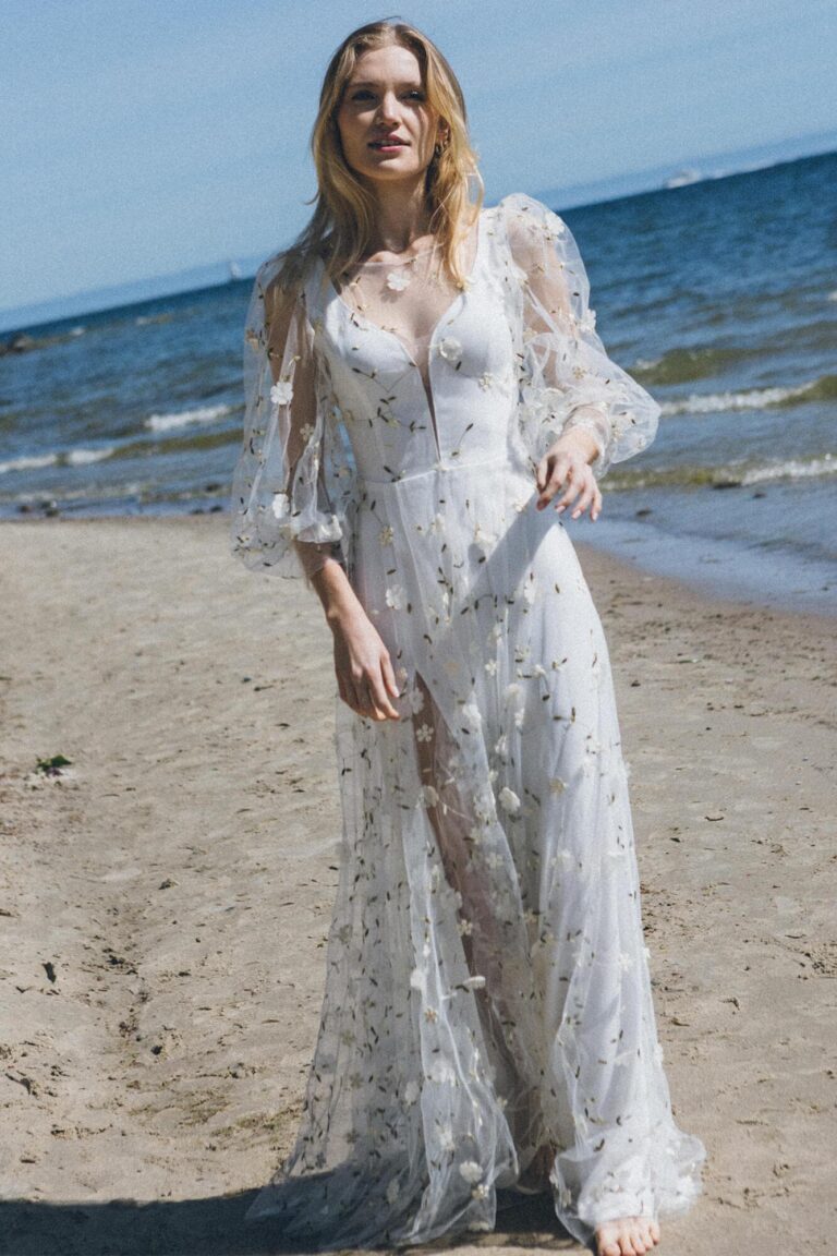 Suknia z długimi rękawami i koronkowymi detalami, widoczna na plaży.