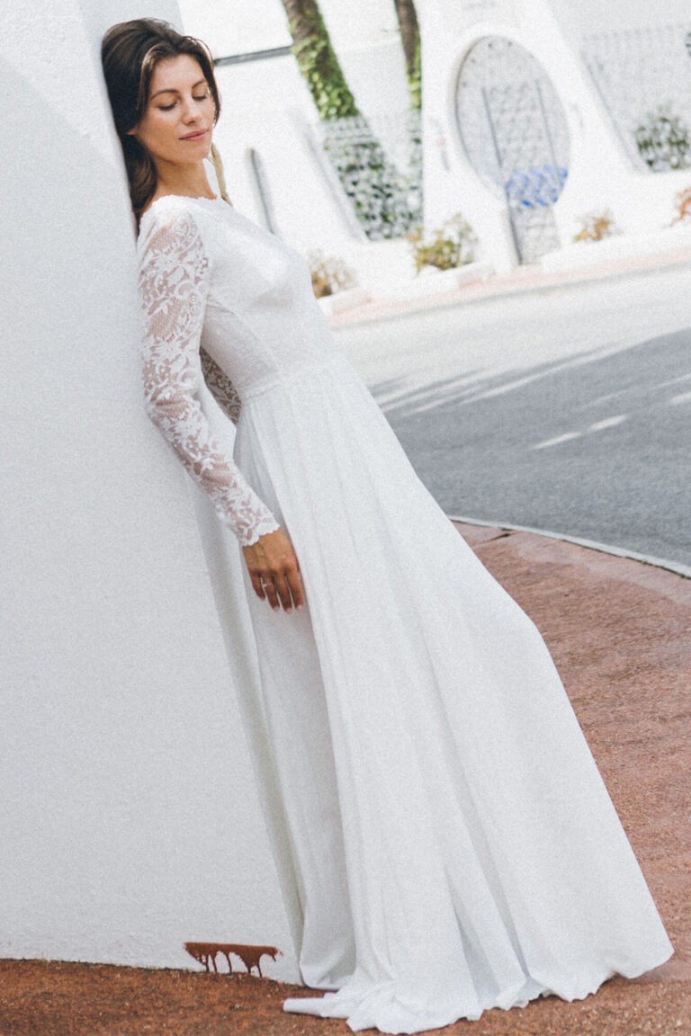 Suknia ślubna z długimi koronkowymi rękawami i rozkloszowanym dołem.