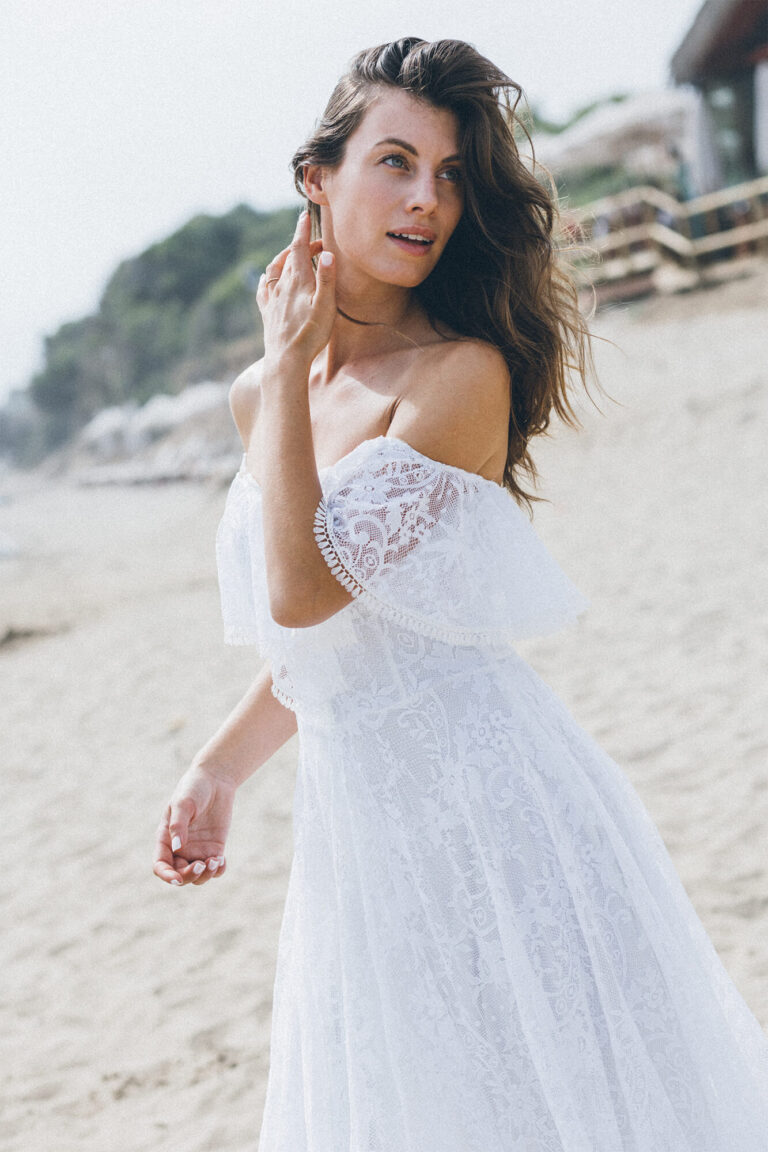 Suknia z odkrytymi ramionami i koronkowymi rękawami w kolorze białym.