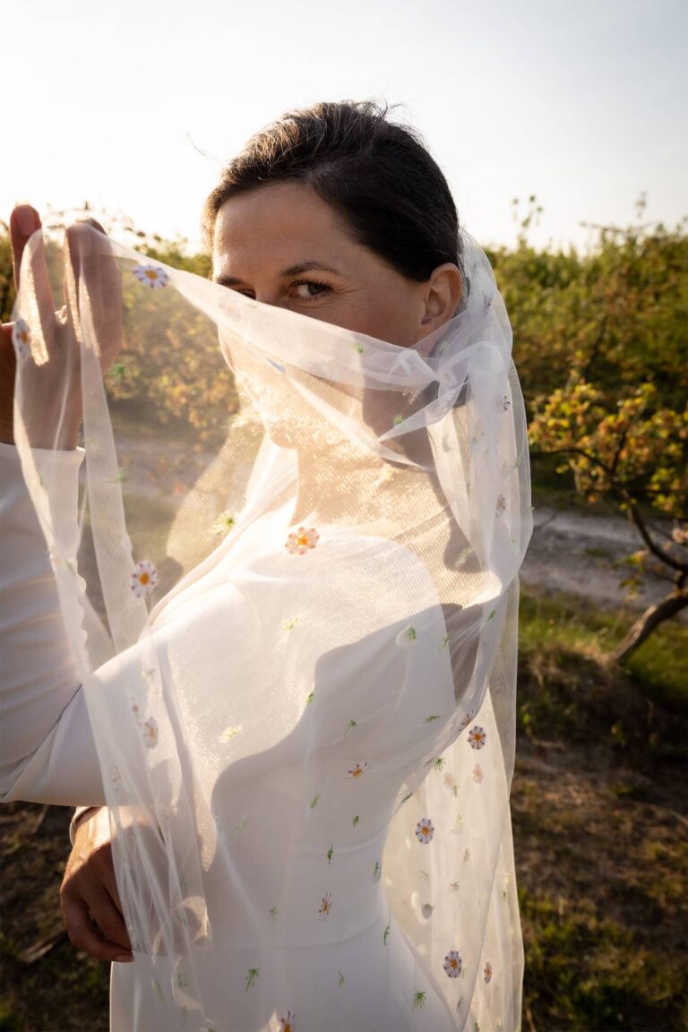 Suknia z długim trenem i koronkowym welonem widziana z przodu.