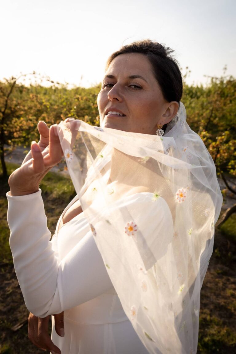 Suknia z długimi rękawami i woalką widoczna w ogrodzie.