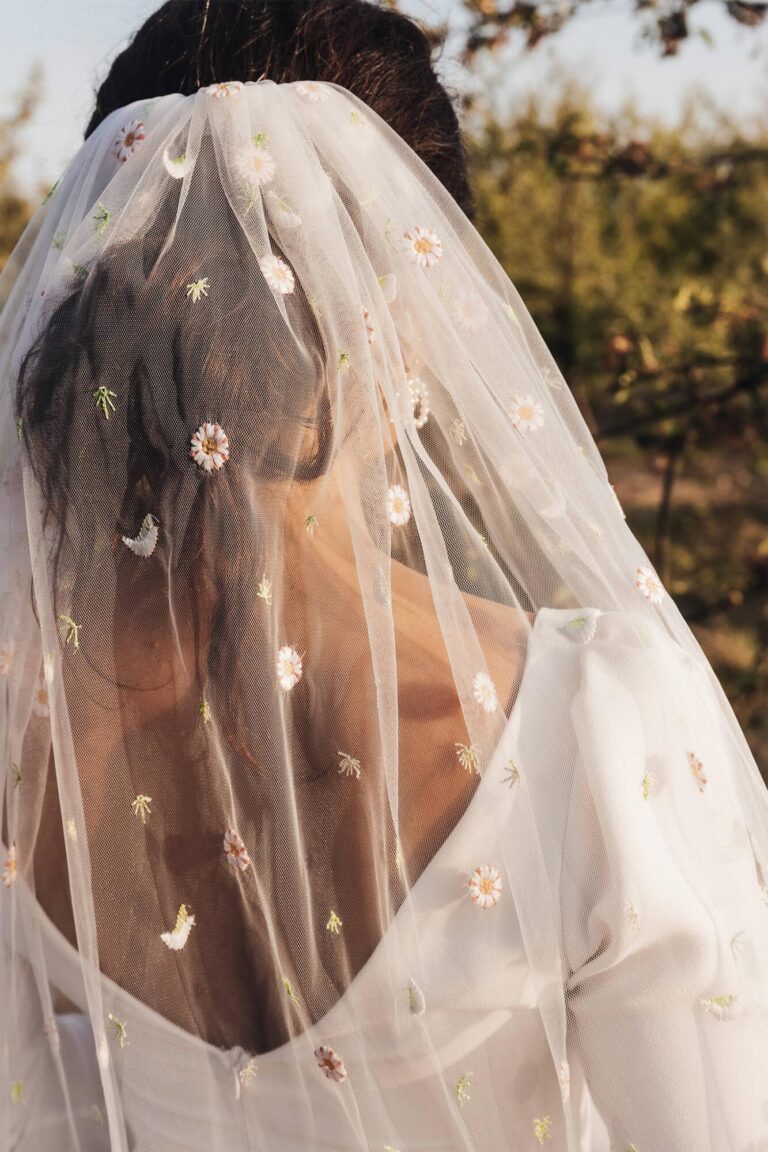 Suknia z odkrytymi plecami i długim welonem z ozdobnymi elementami.