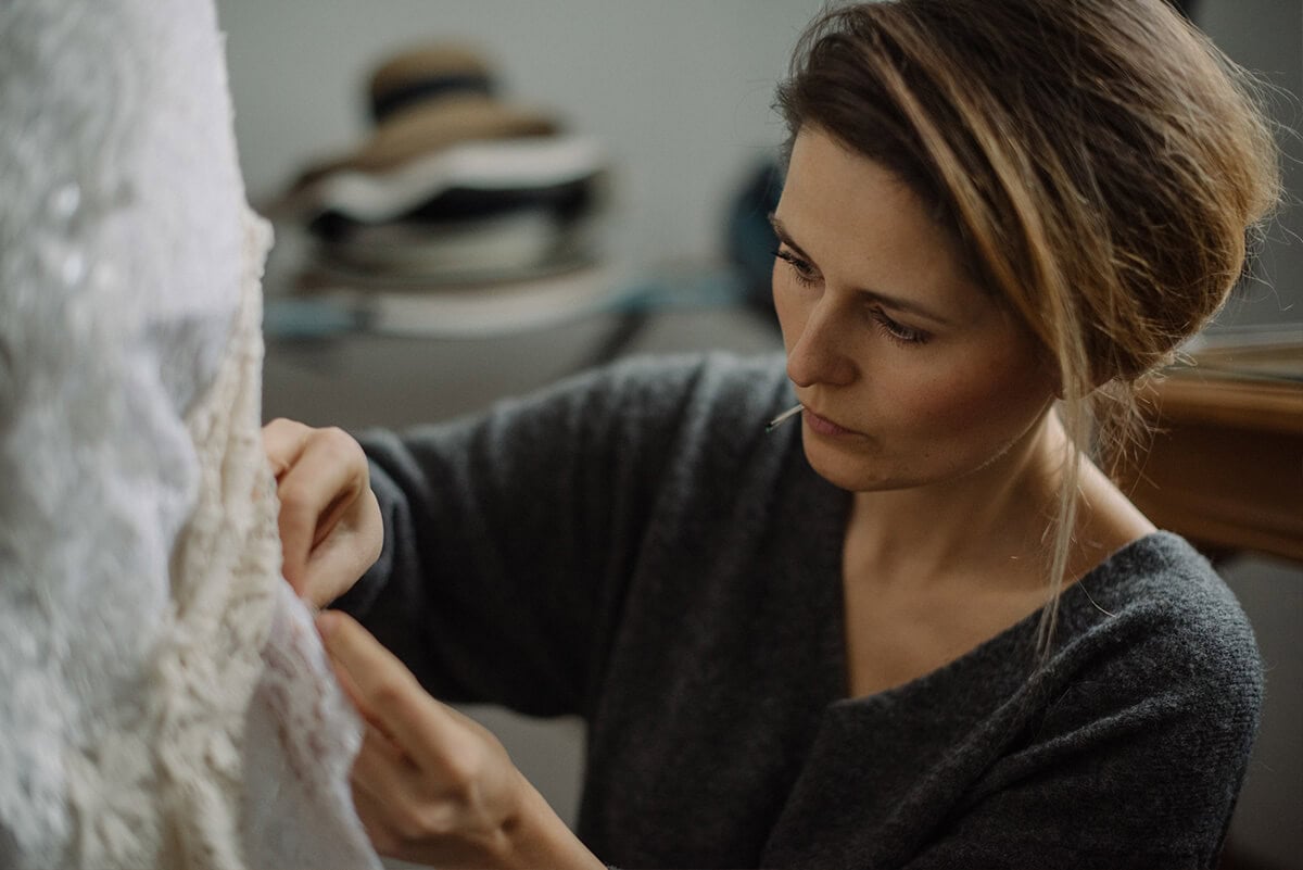 Kobieta pracuje nad detalem białej sukni ślubnej w pracowni krawieckiej.