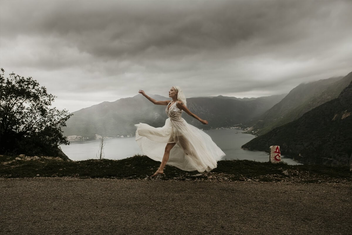 suknia ślubna z długim, zwiewnym dołem, kobieta tańcząca na tle górskiego krajobrazu i jeziora