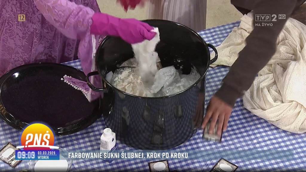 Osoba w różowych rękawiczkach trzyma materiał, wkładając go do czarnego garnka z wodą.